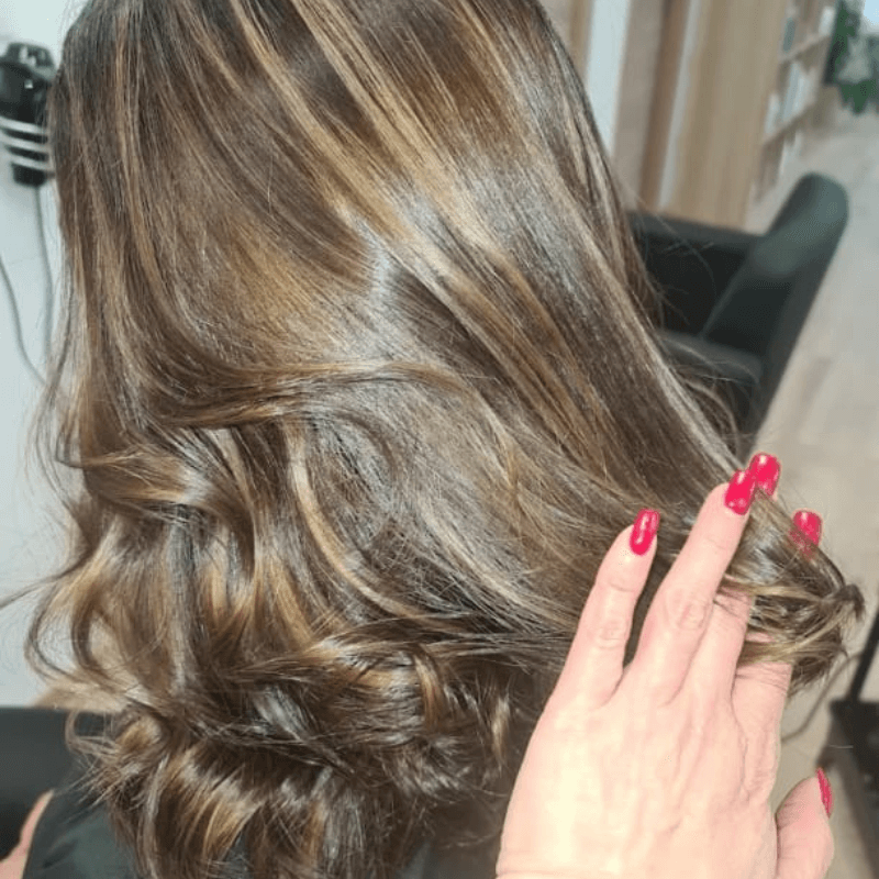 Cabello algo rizado bien peinado y una mano acariaciando las puntas